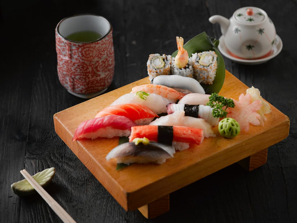 Ten pieces of assorted nigiri and three pieces of rolled sushi lay upon a Japanese wooden tray as someone visits a sushi restaurant as one of the things they do in Nara
