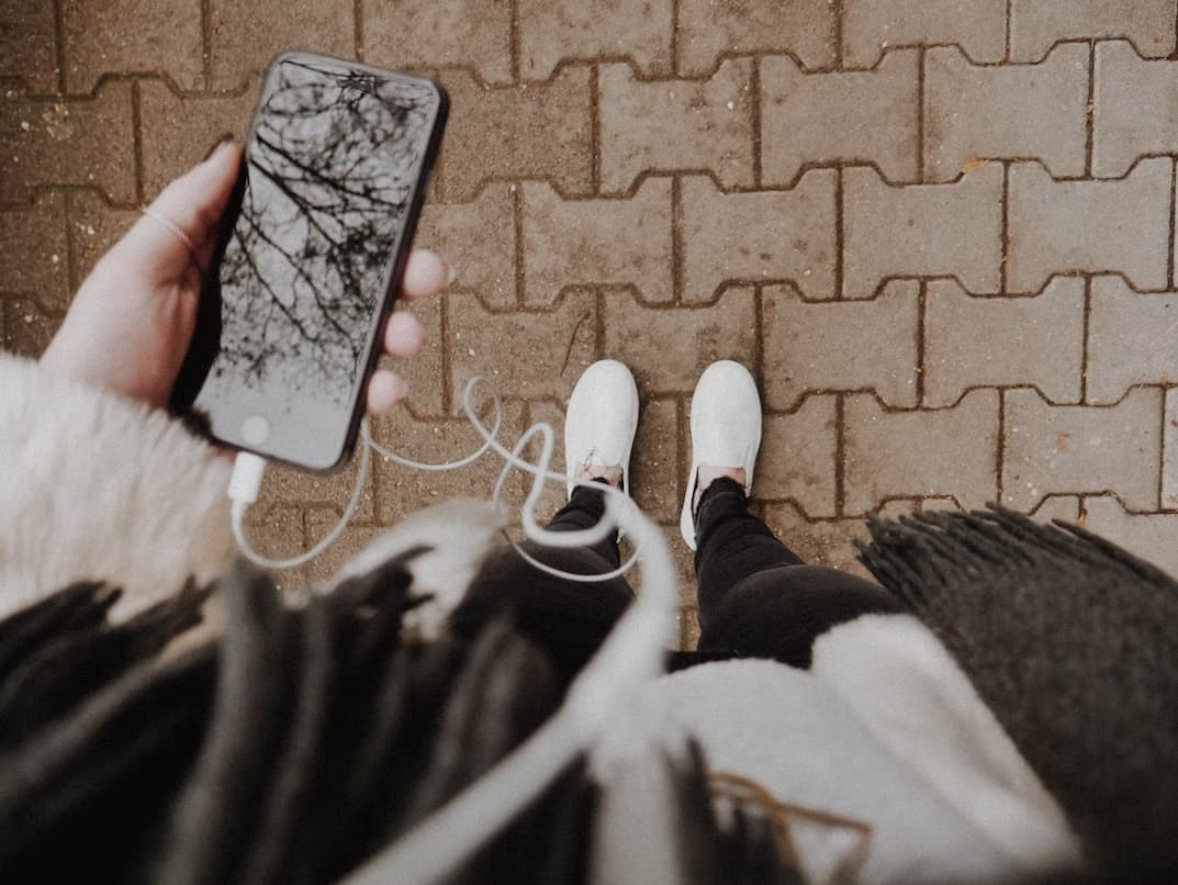 A girl looks down and looks at her cellphone with earbuds attached as she listens to a podcast in Japan
