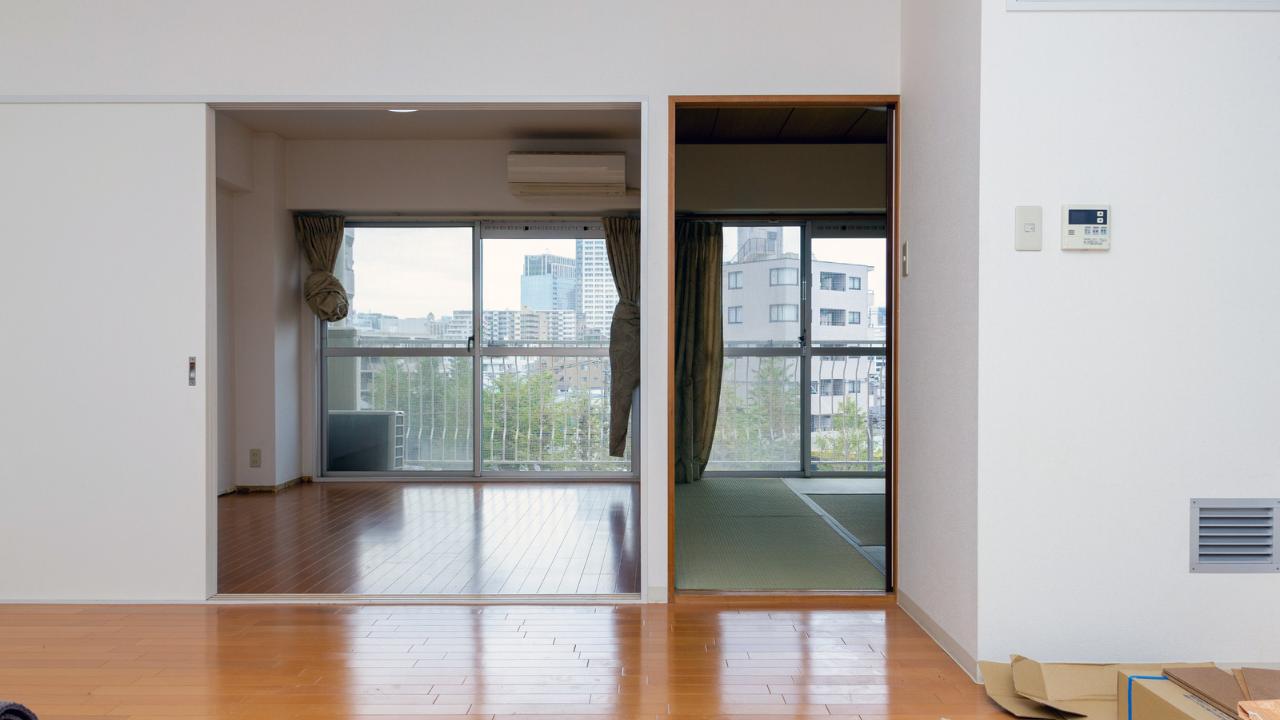 Rental property in Tokyo showing main room and doors leading to separate bedroom and room with tatami mat floors with large doors leading to the outside balcony