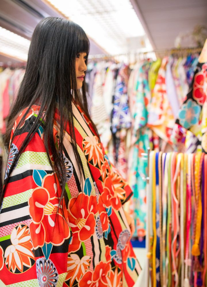 Japanese woman trying on a red kimono with an intricate design in a kimono rental store