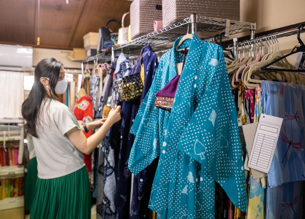 Young woman looking at three kimono in blue, white, and teal in a kimono rental shop