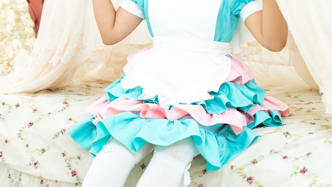 Visiting a maid cafe in Tokyo and a maid is sitting on a big beige sofa wearing a light teal dress with pink and white frills