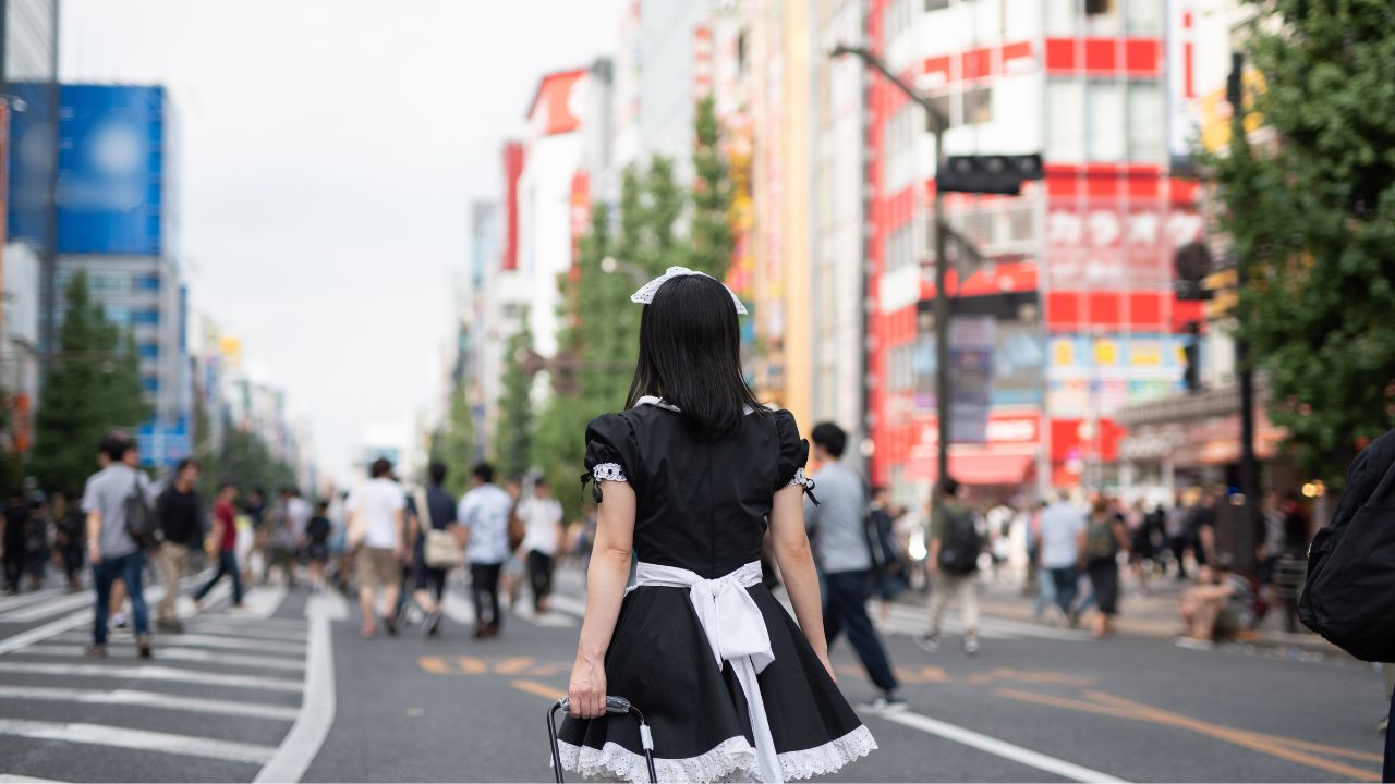 A maid standing with her back facing the camera on the streets of Akihabra advertising a maid cafe