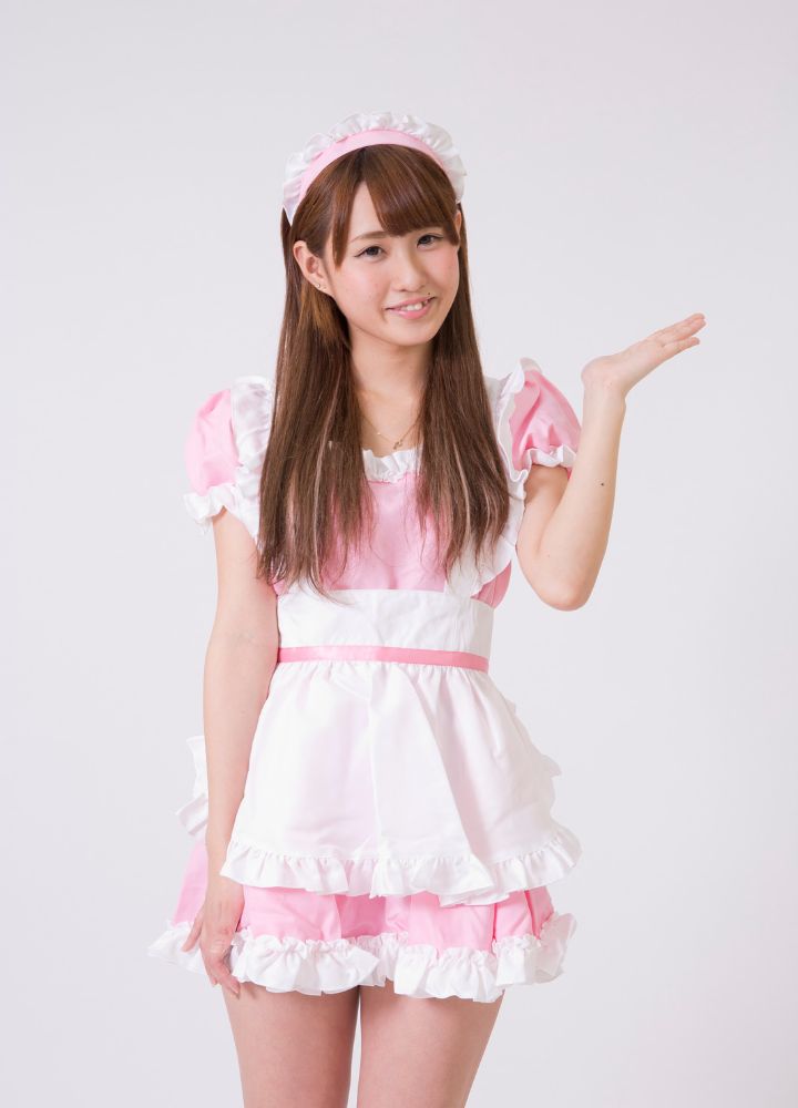 Japanese girl in in a pink and white maid cafe outfit holding up her hand and waving