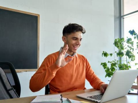 Man waving at laptop during zoom meeting