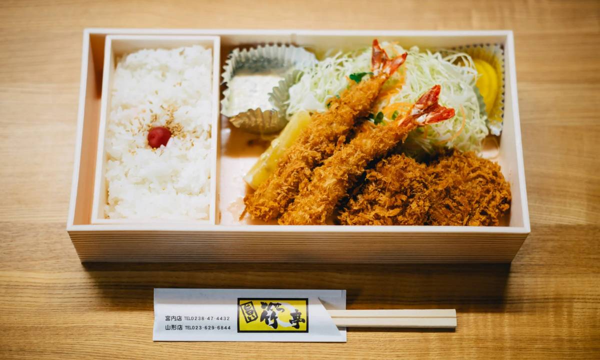 Fancy wooden bento box with fried shrimp, rice, and more
