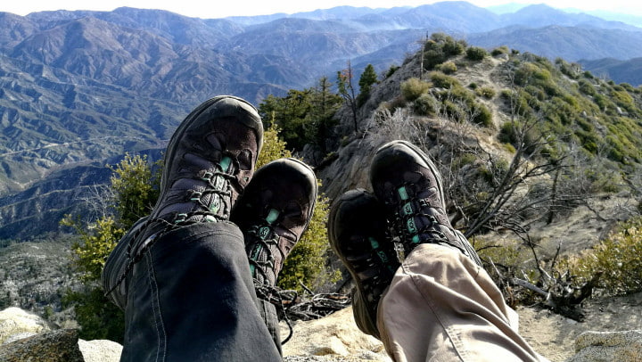 Two sets of feet overhanging a mountain summit