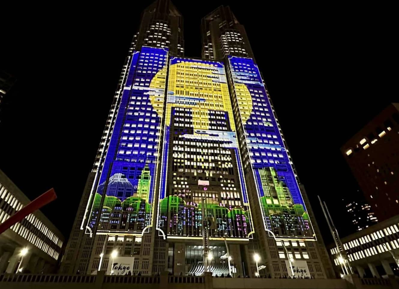 A tall skyscraper with a sun and sky illustration projected on it in Shinjuku at night