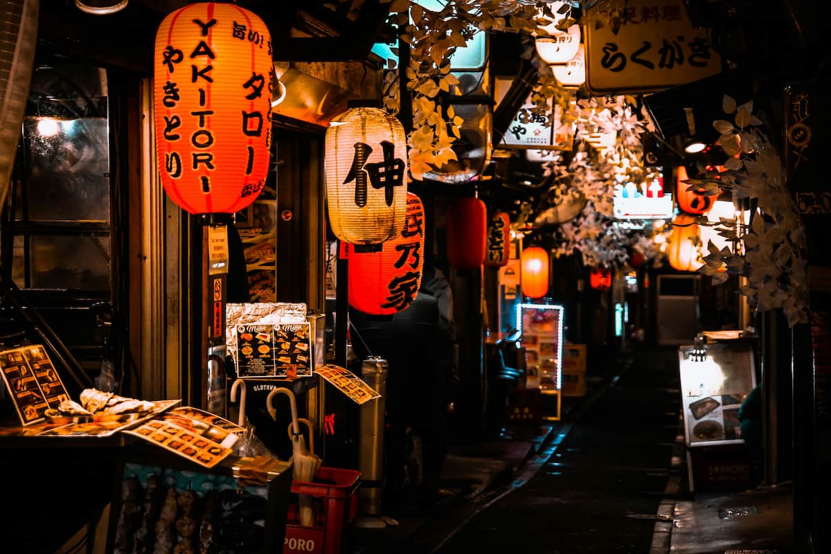 A narrow street in Shinjuku with small restaurants and Japanese lanterns at night