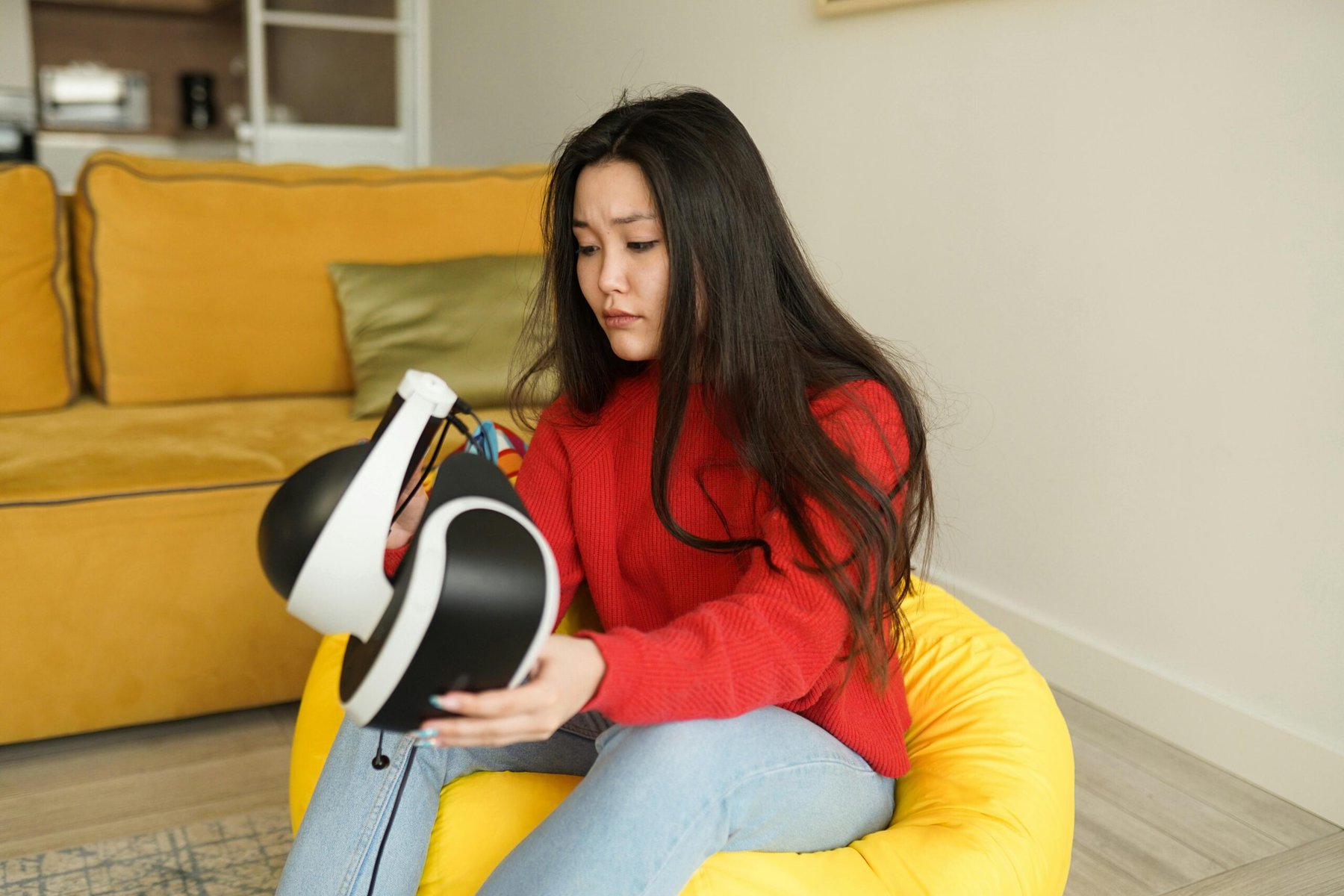 Woman sitting on bean bag in her home and holding a VR headset