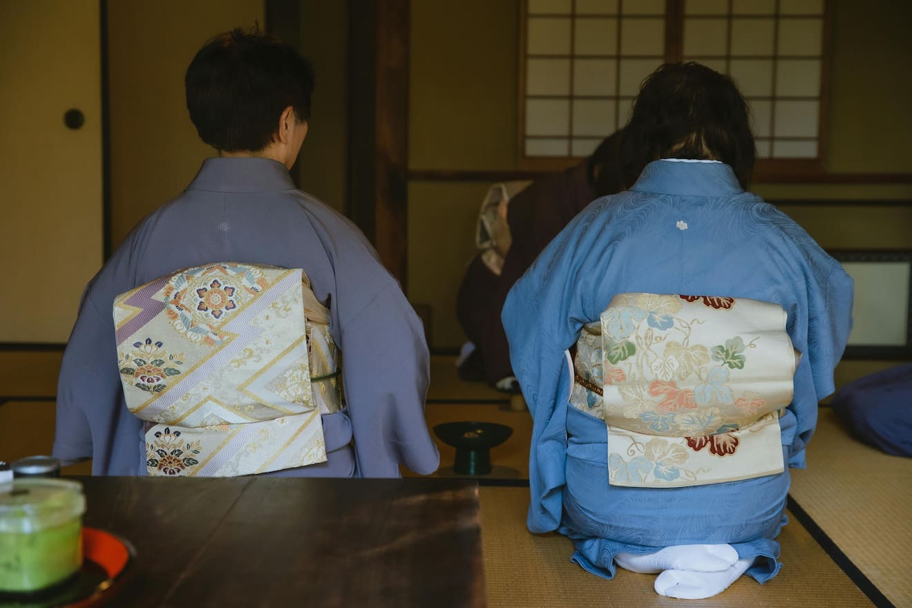 Japanese people wearing kimonos while sitting on a tatami mat and drinking tea.