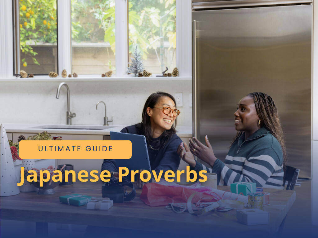 Two women, one Asian and the other African, talking by the table in the kitchen, laughing.