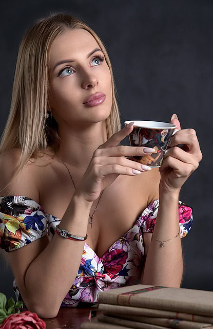 A woman in western style makeup holding a tea cup while looking up thinking