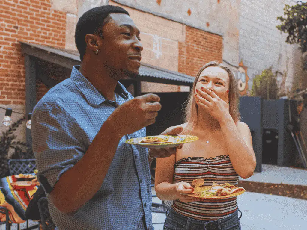 A man and a woman eating the best Mexican food in Tokyo while standing, smiling and laughing.