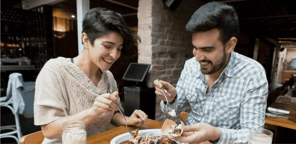 A man and a woman eating the best Mexican food in Tokyo at a restaurant while smiling and taking their food.
