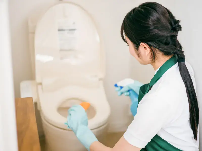 Woman cleaning a Japanese toilet with gloves and spray