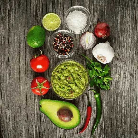 An image of guacamole and it's ingredients surrounding it such as avocado, tomato, cilantro, etc. as the best Mexican food in tokyo