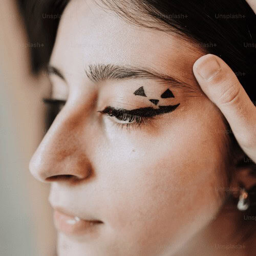 A face of a woman with showing the eyeliner on her left eye with a with two triangular designs on her eyelids