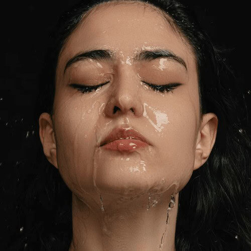 A face of a woman wearing a light makeup with water dripping on her face